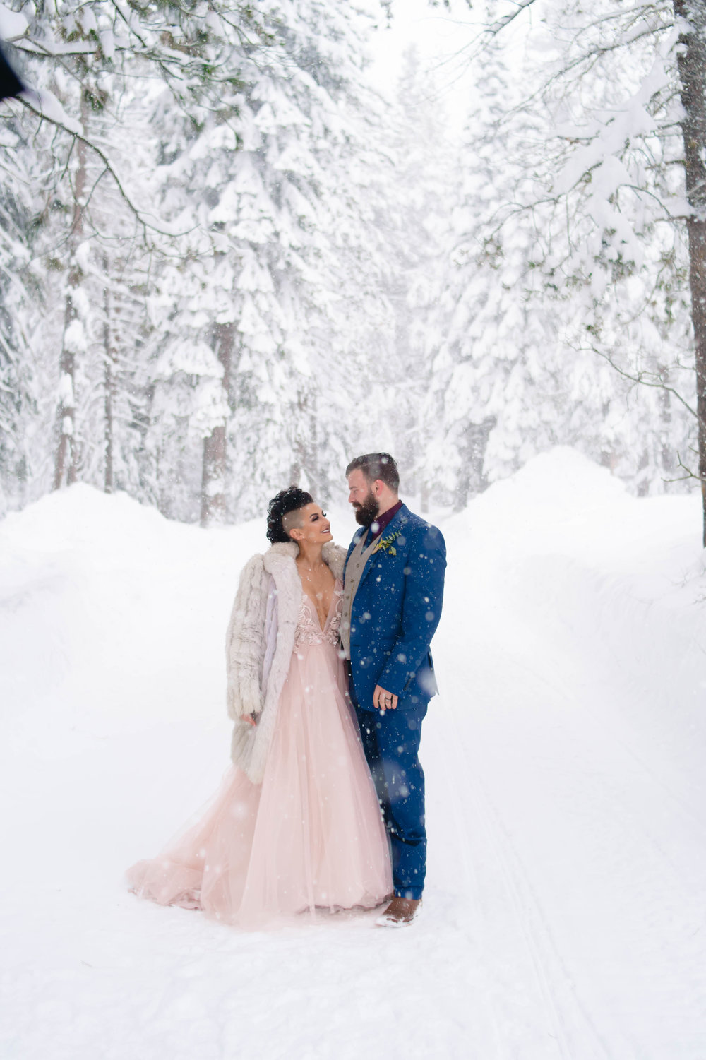 photo of a blush wedding gown and blue suit with the bride and groom during snowfall