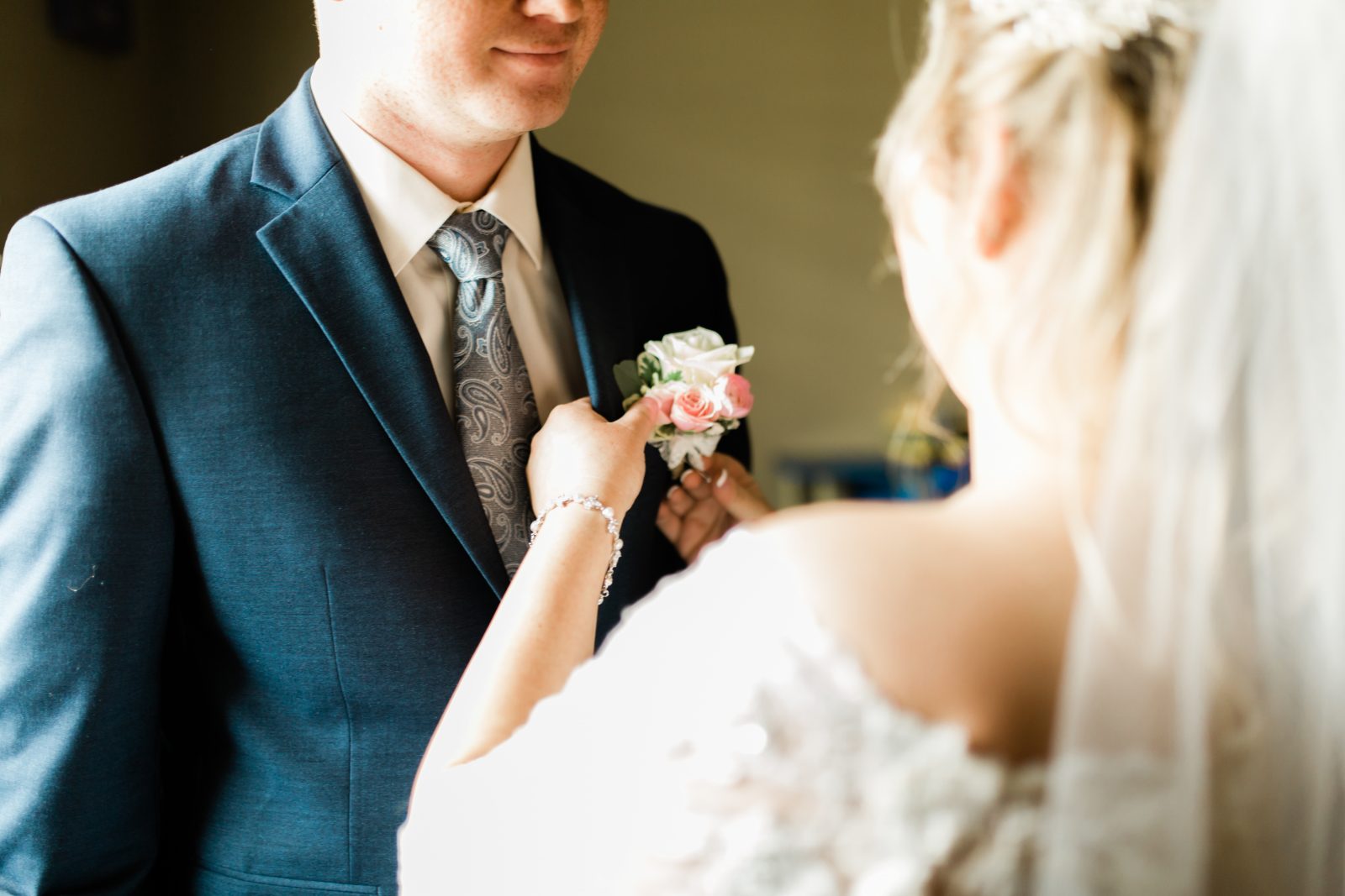 bride pinning the boutonniere on the groom's blue suit