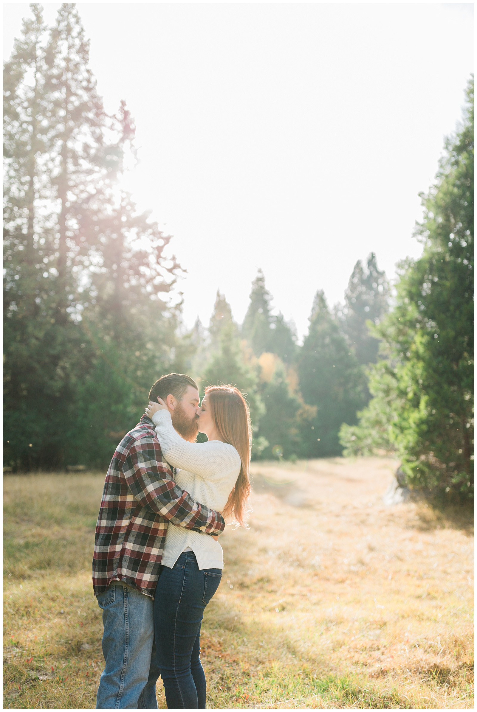 couple kissing for fall engagement photos in a meadow
