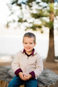 young boy sitting on a rock during a fall family photo session at shaver lake