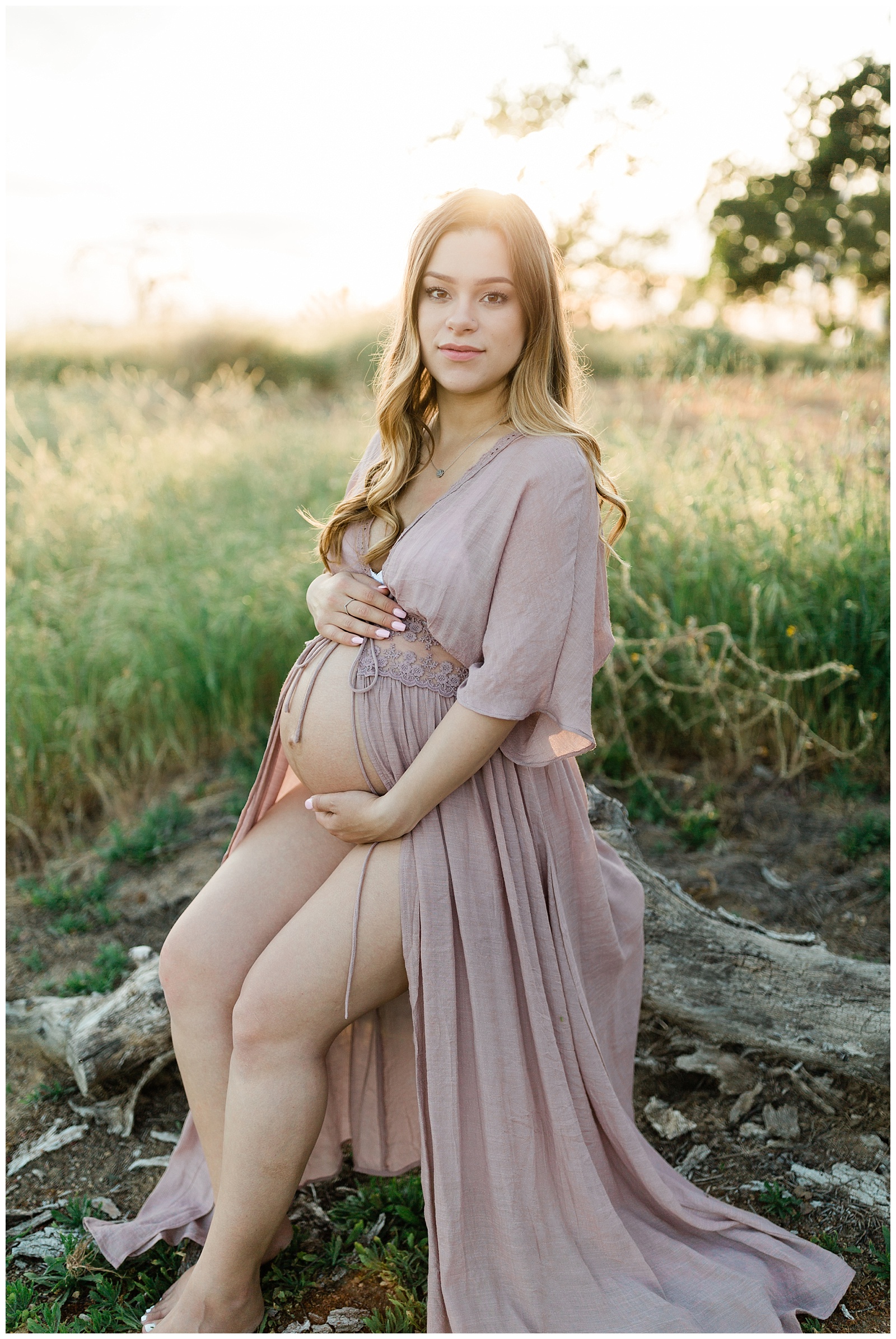  pregnant woman in a grassy field and sunset wearing a blush pink open belly dress