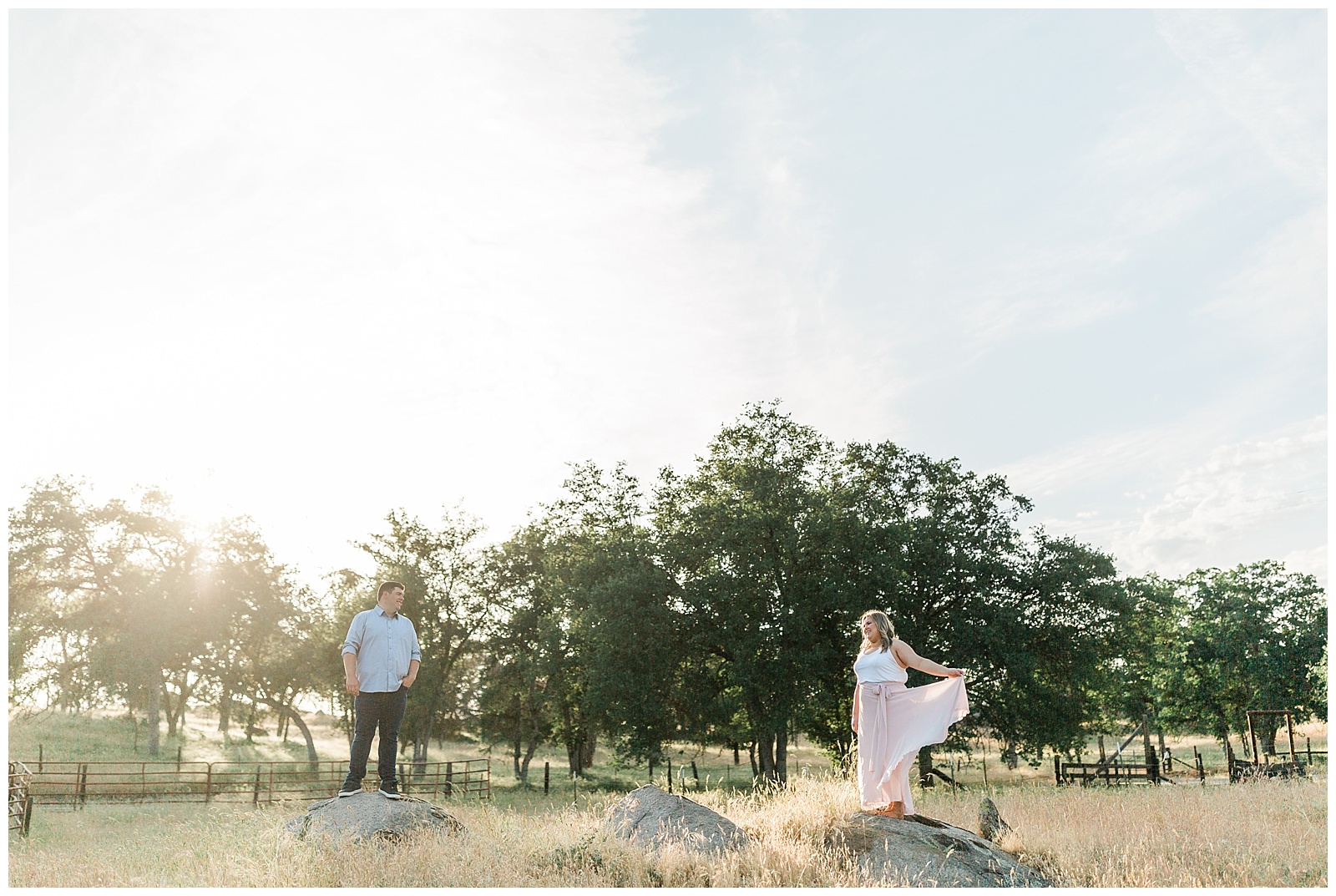 newly engaged couple standing on rocks in front of oak trees at sunset