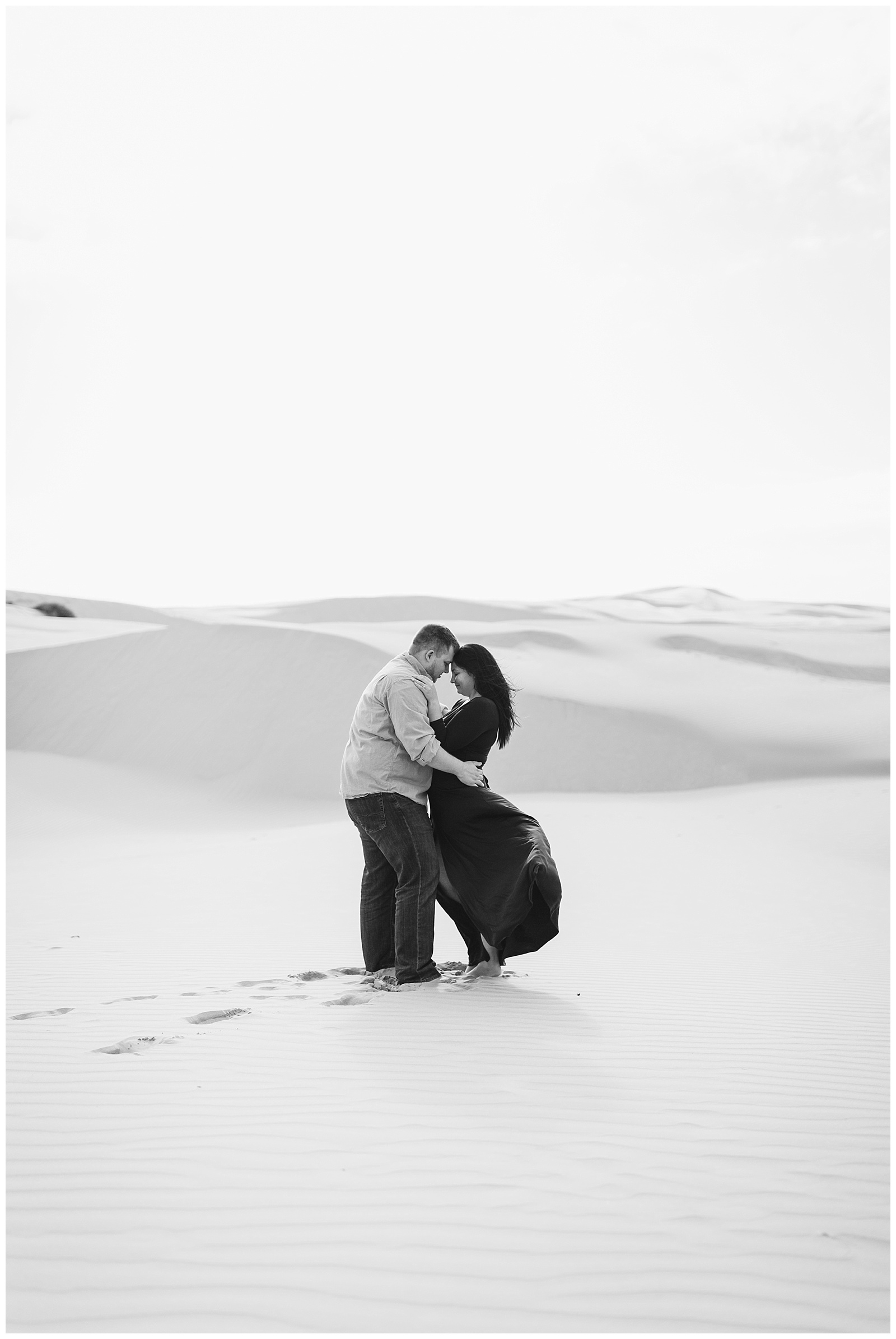 intimate black and white photo of a couple embracing on the windy pismo beach dunes