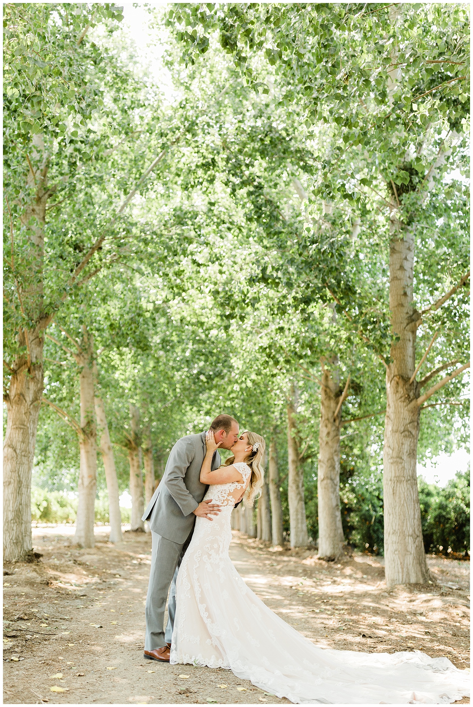 bride and groom kissing on their wedding day on a driveway lined with trees
