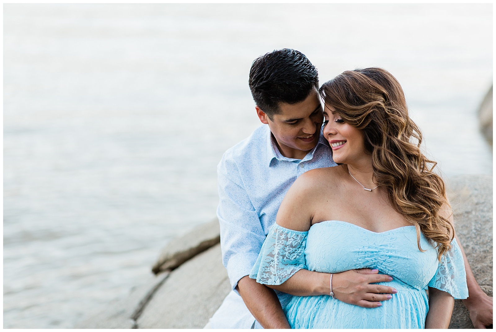 couple sitting on a rock lakeside for a maternity portrait