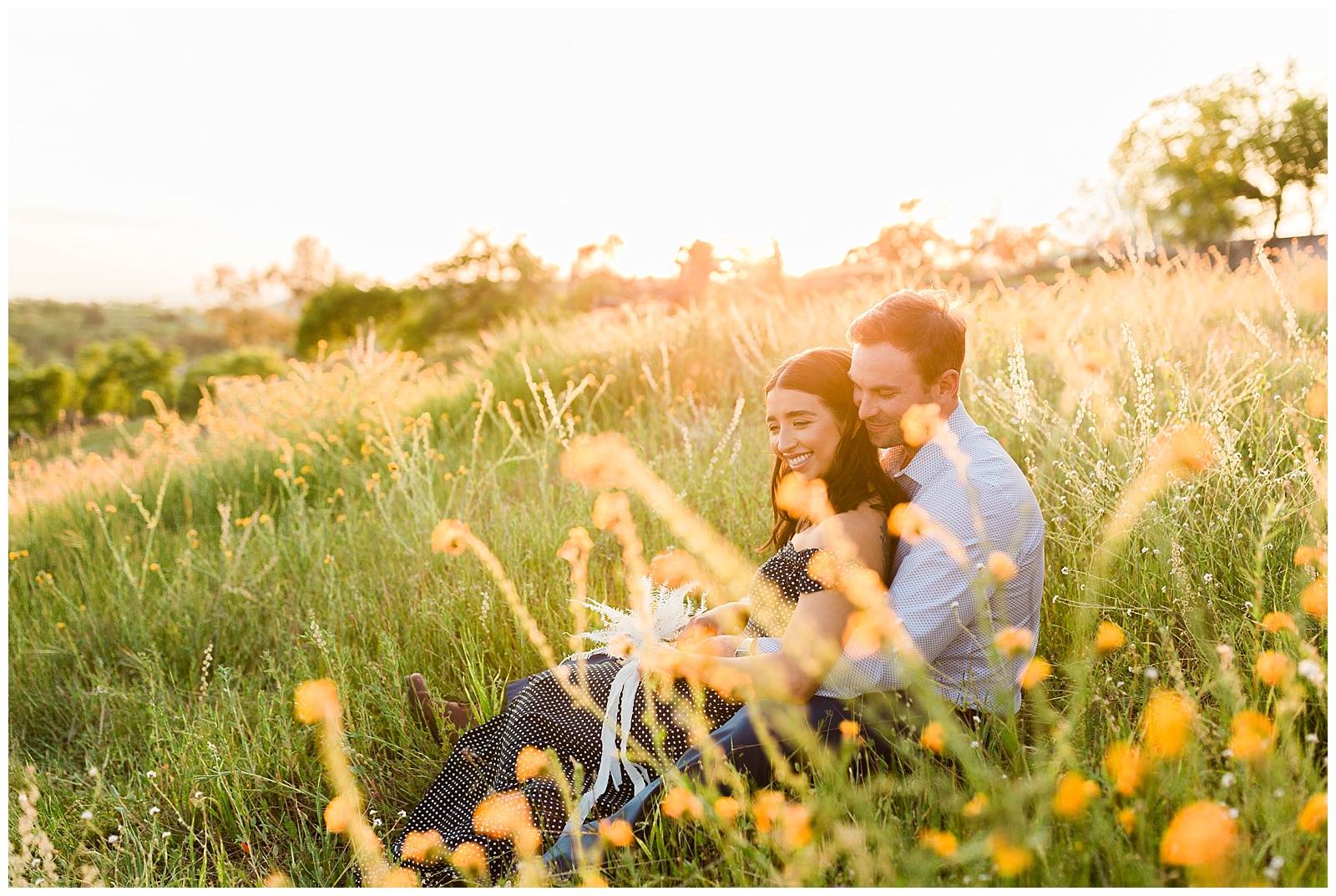 couple sitting and hugging in a wildflower field as the sun sets over the hills of fresno for a styled shoot