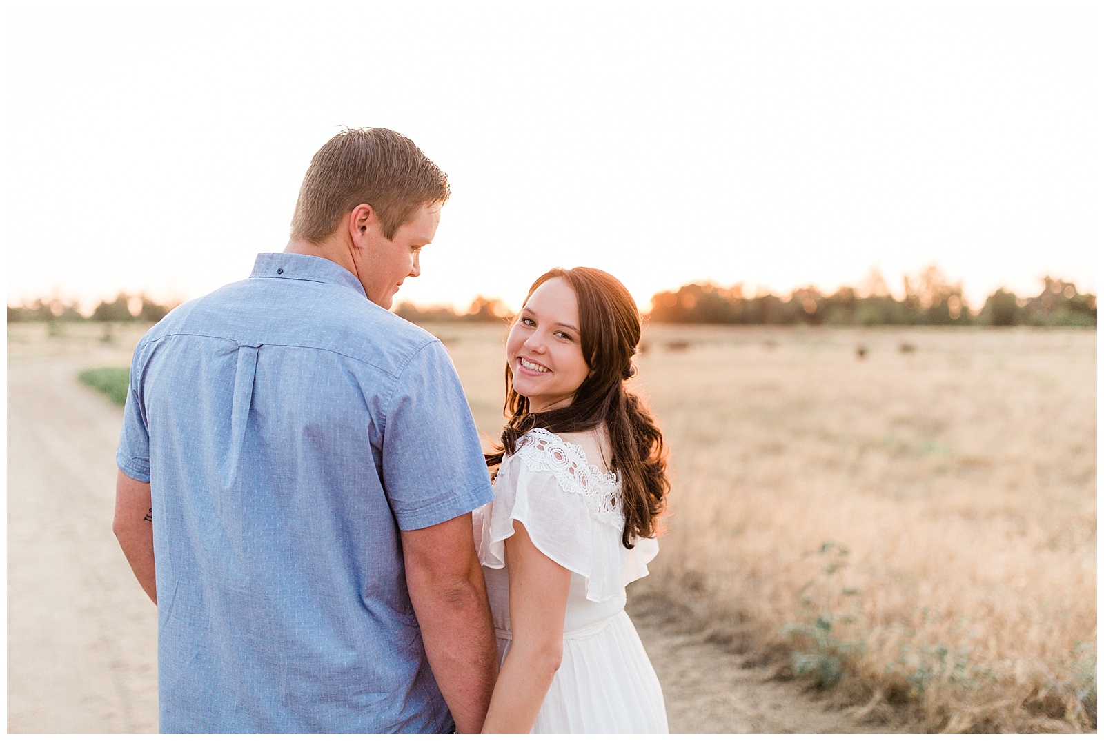 engaged couple in an open field at sunset smiling for engagement photos