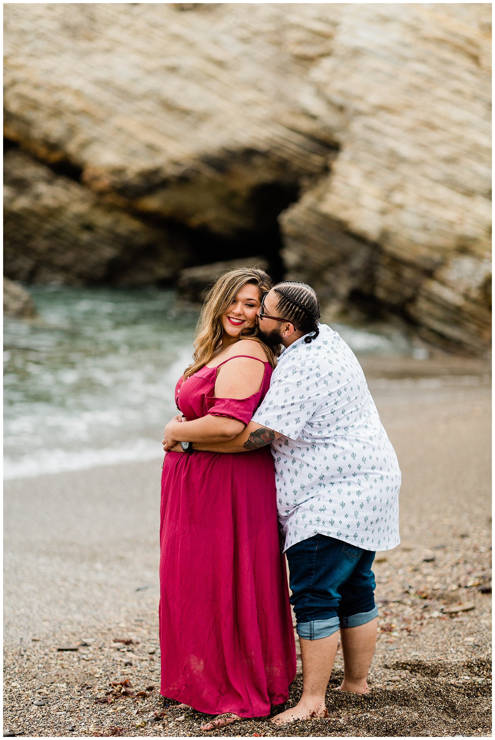 engaged couple standing near the ocean hugging and kissing