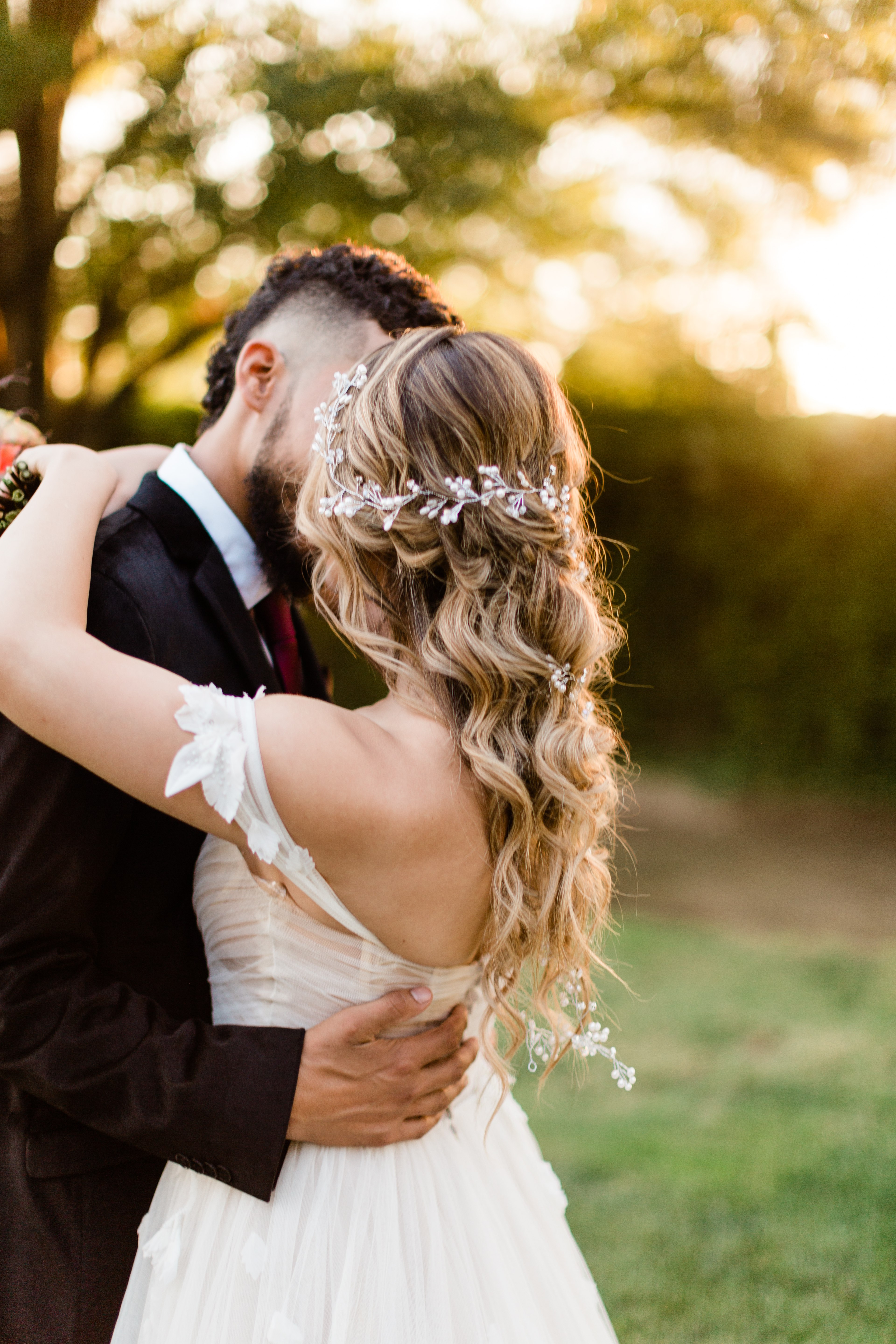 bride with long flowing hair and a jeweled bridal hairpiece kissing her groom at sunset