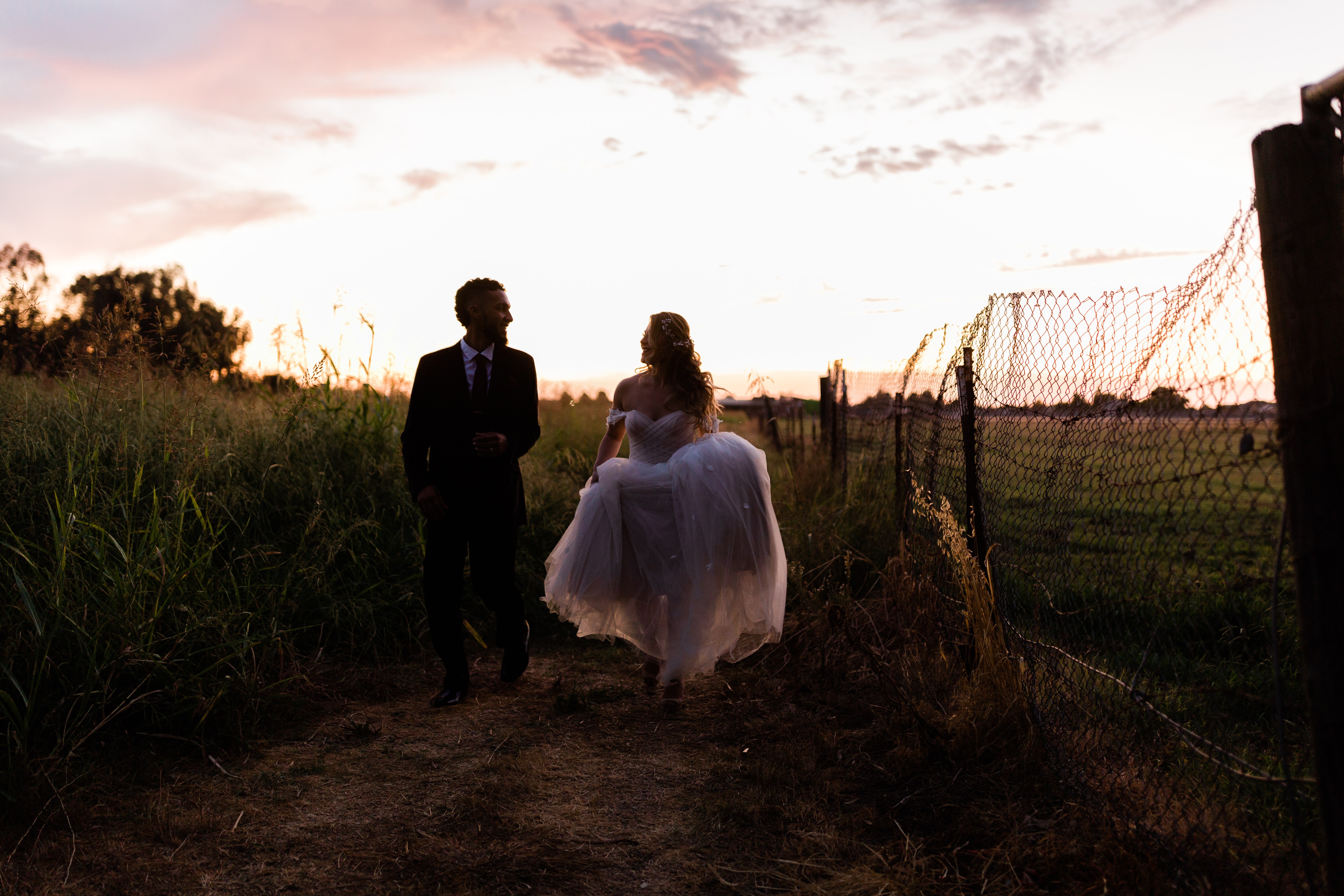 bride and groom running through a field under a purple sunset