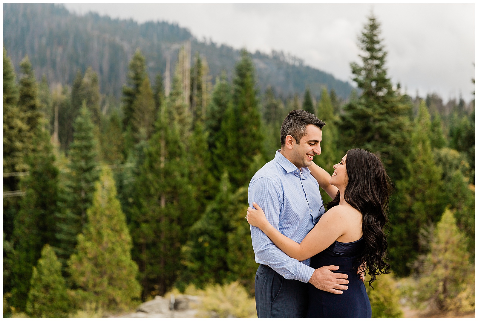 engaged couple dancing and smiling on a large rock in the mountains