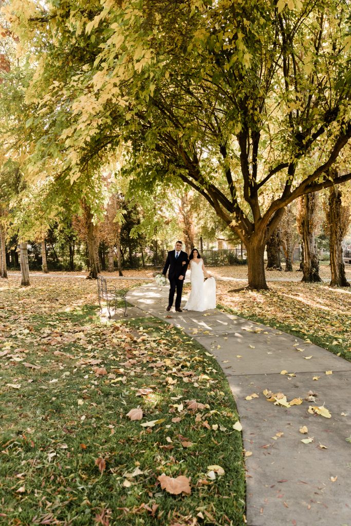 bridal couple walking down tree path with fall leaves