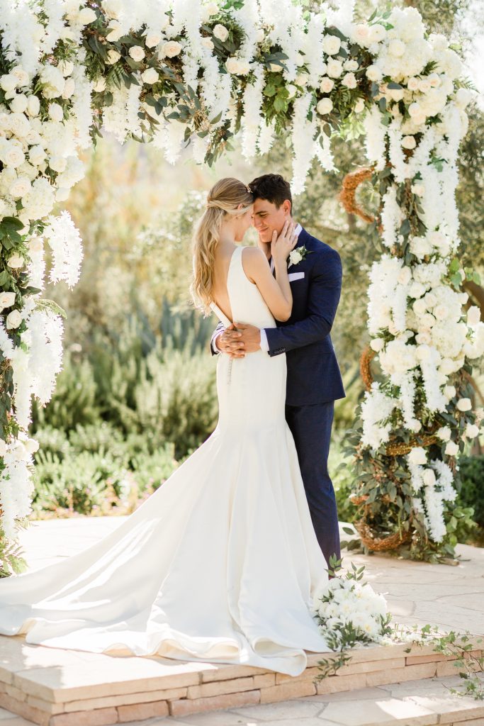 bride and groom hugging at outdoor ceremony with cascading white flowers