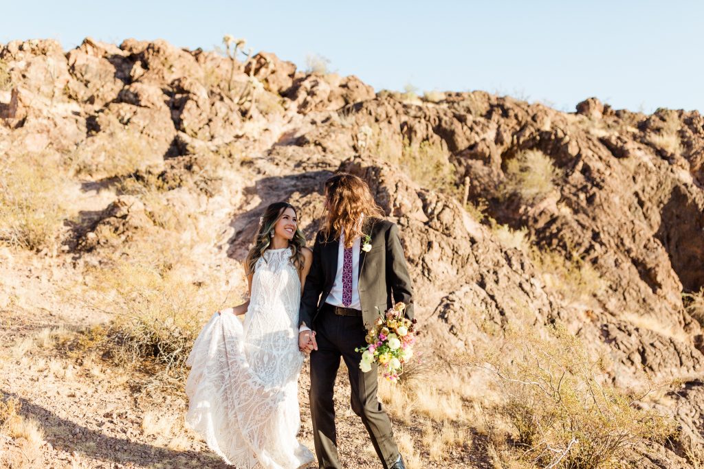 bohemian wedding couple holding hands and walking through the desert