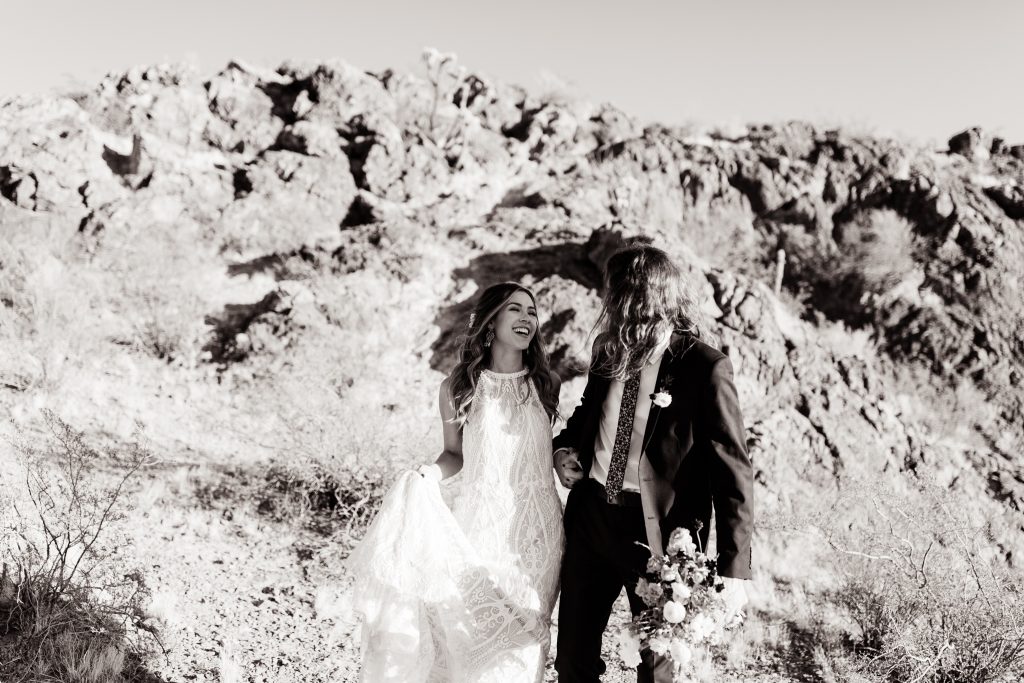 black and white of a newly married couple holding hands and walking through the desert