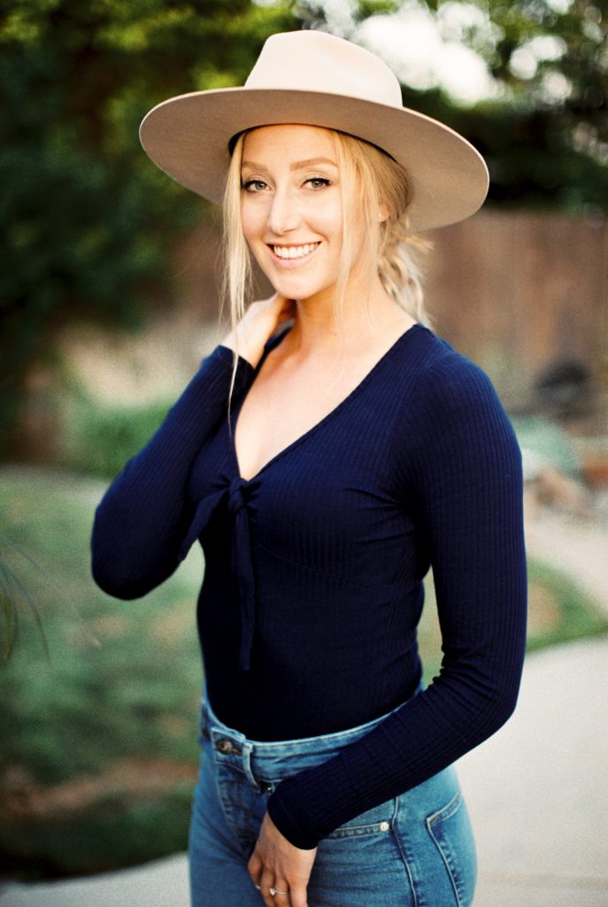 woman smiling while wearing a beige suede hat, navy blue shirt and high waisted jeans