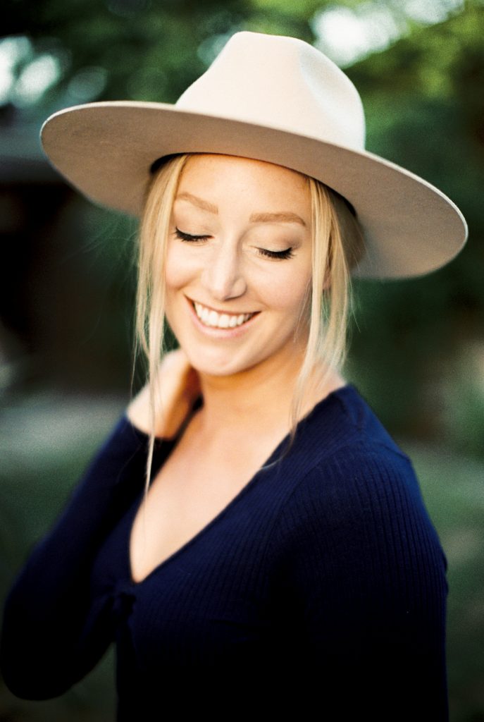 film portrait of a blonde woman smiling while wearing a beige suede hat and a navy blue shirt