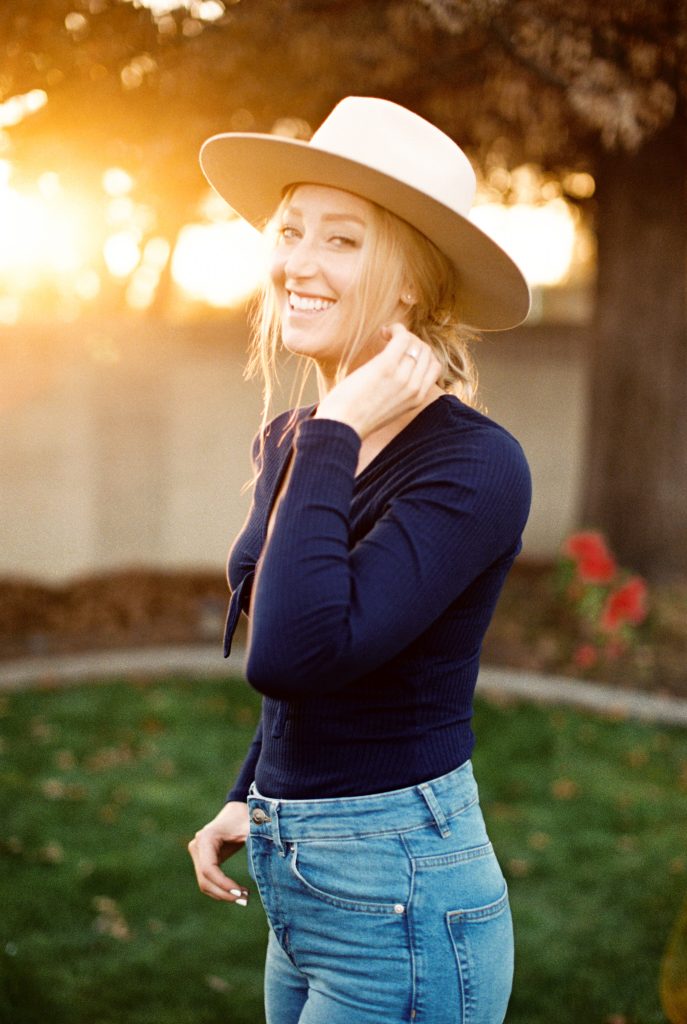 woman laughing and smiling while wearing a beige suede hat and high waisted jeans