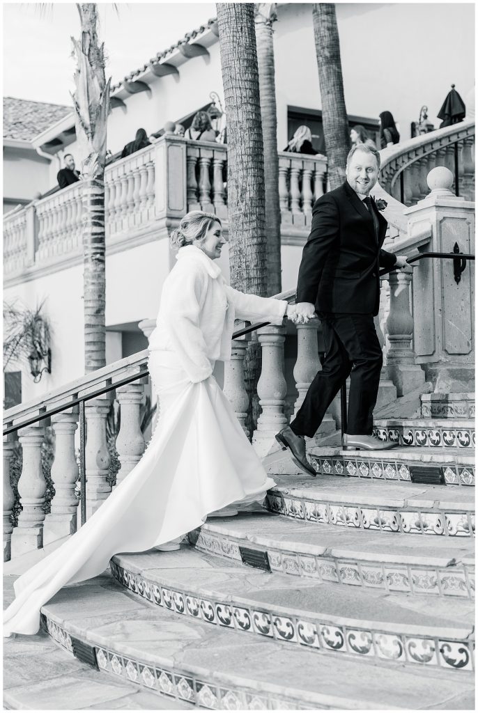 black and white of groom walking bride up stairs in a white fur jacket
