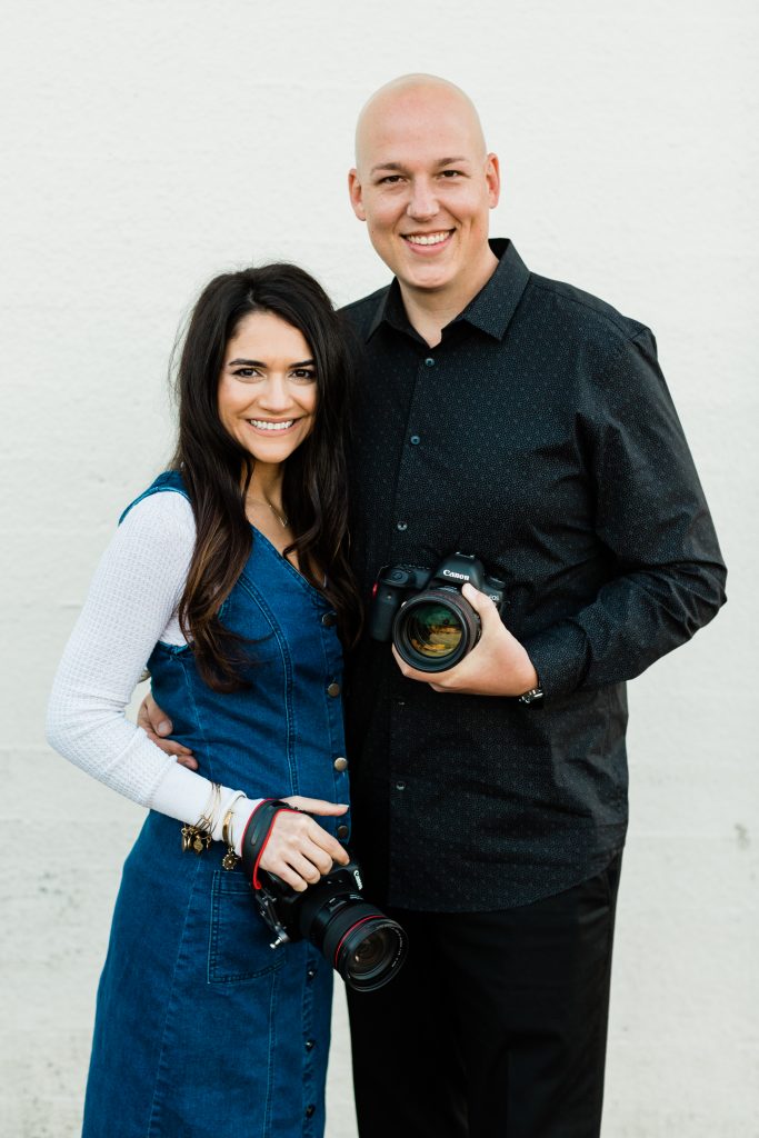 husband and wife photography team holding their cameras and smiling