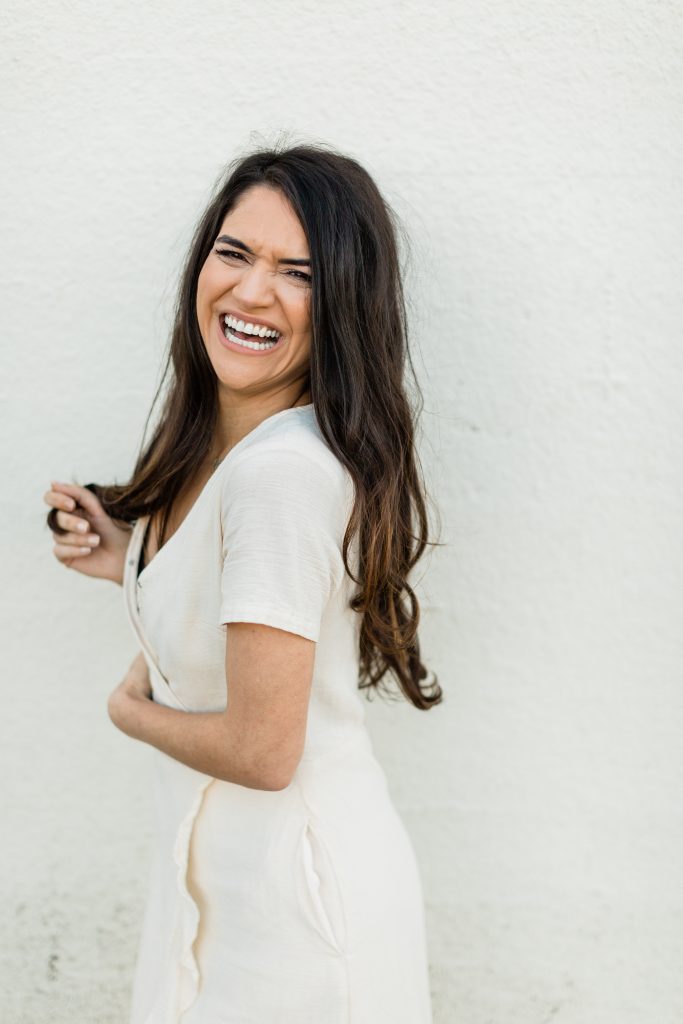 woman with long dark brown hair laughing and smiling while wearing an ivory wrap dress
