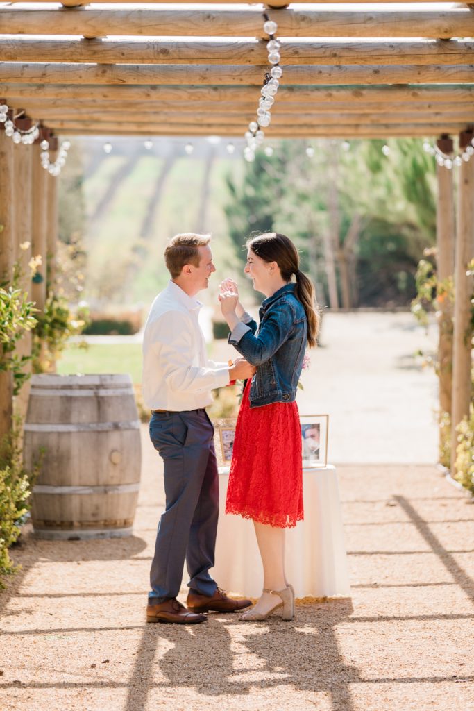 couple excitedly standing together under a wooden archway as the man gets ready to surprise her with a marriage proposal