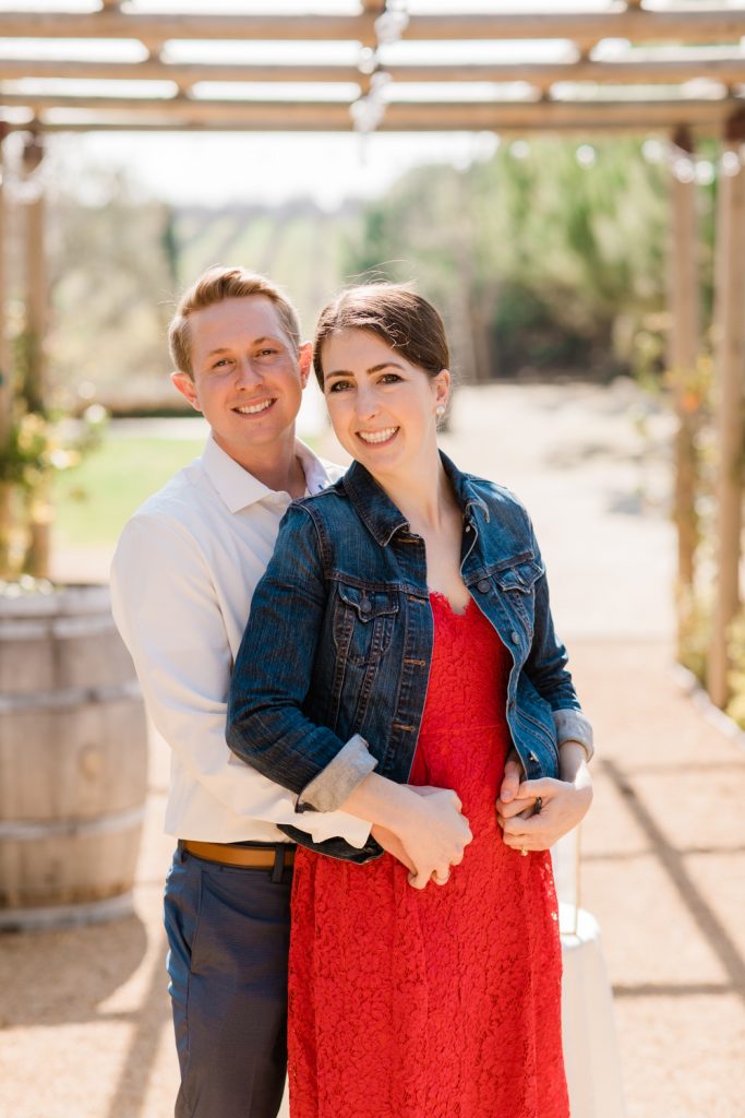 newly engaged couple posing in a red lace dress and denim jacket and white button up shirt and navy slacks