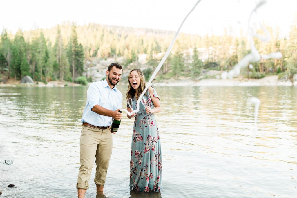 champagne popping with an engaged couple standing along the shores of shaver lake in california