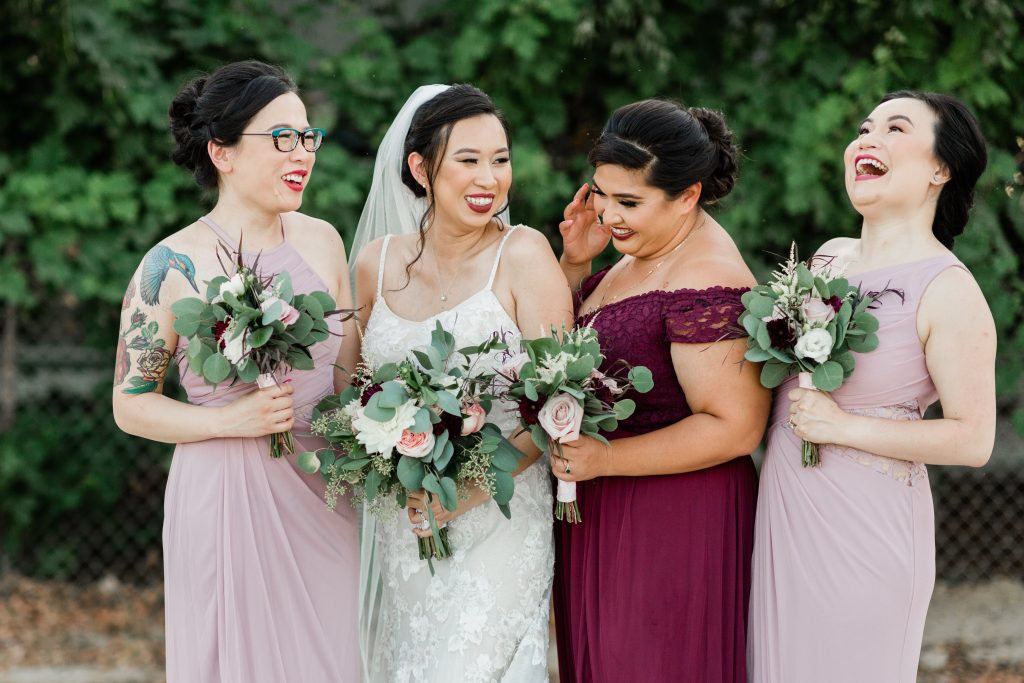 bride and her bridesmaids smiling and laughing together while they hold their bouquets