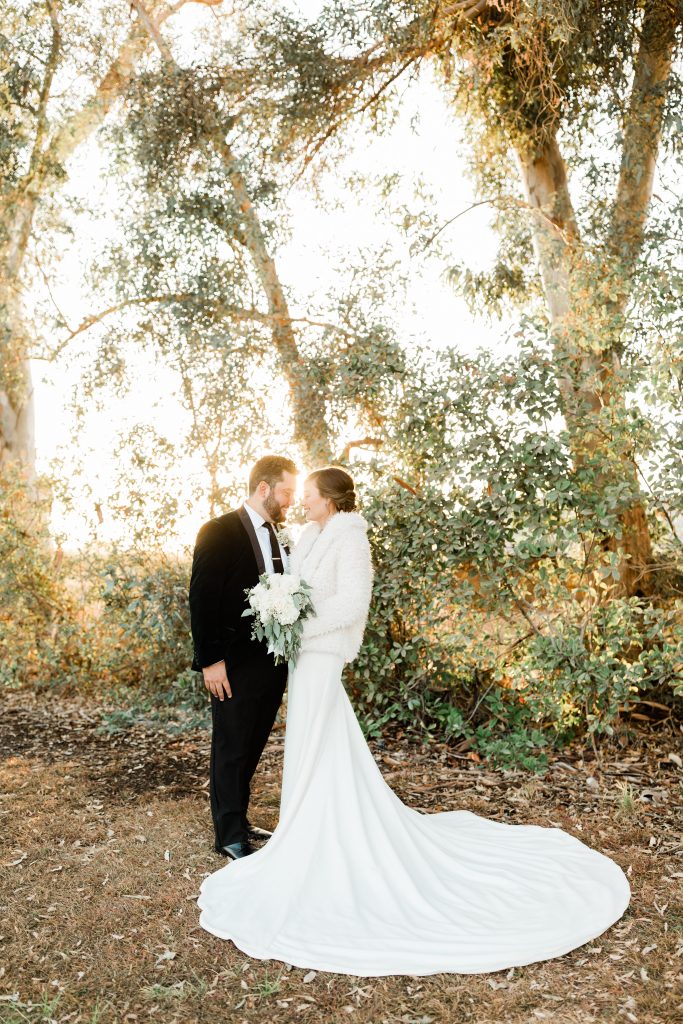Couple near eucalyptus with bride in fuzzy coat at sunset