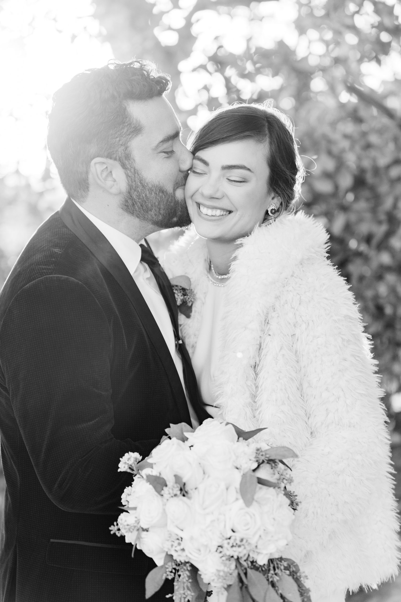 black and white image groom kissing bride on cheek smiling