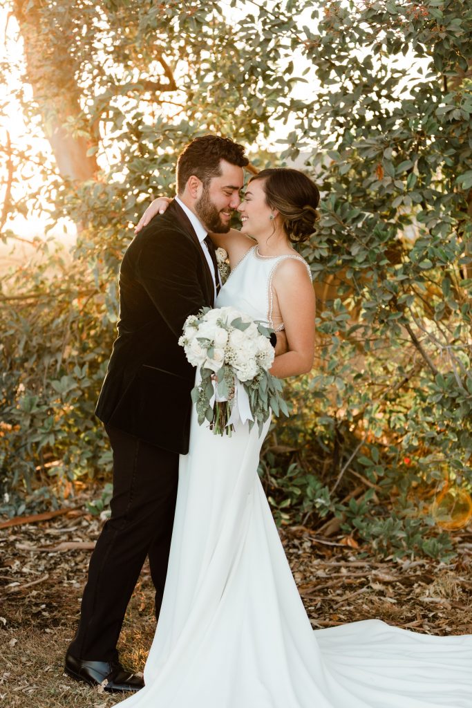Bride and groom hugging while holding white rose and eucalyptus bouquet