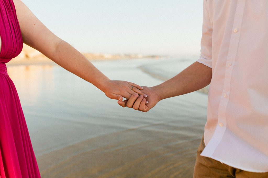 engaged couple holding hands on the beach