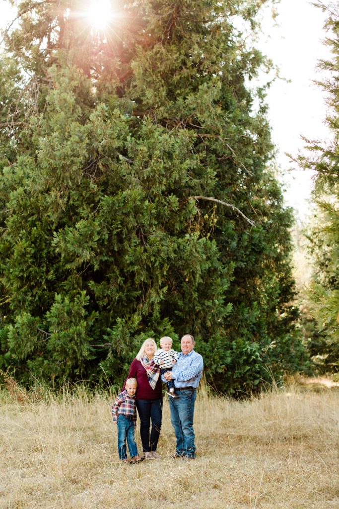 family standing in a meadow of dried grasses with evergreen trees and wearing maroon and blue outfits