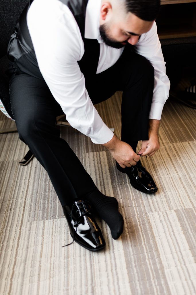 man in a black suit tying black dress shoes