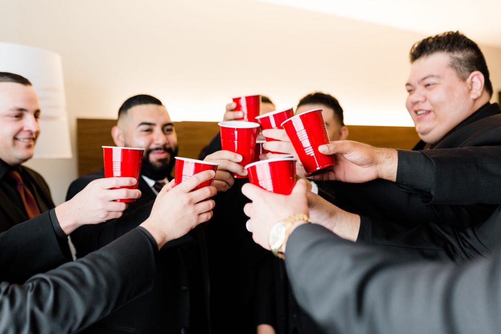 groom and groomsmen cheering before taking shots out of red solo cups