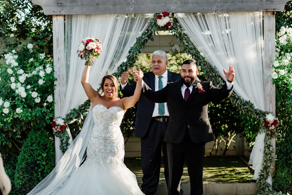 excited bride and groom after their wedding ceremony holding their hands up in celebration