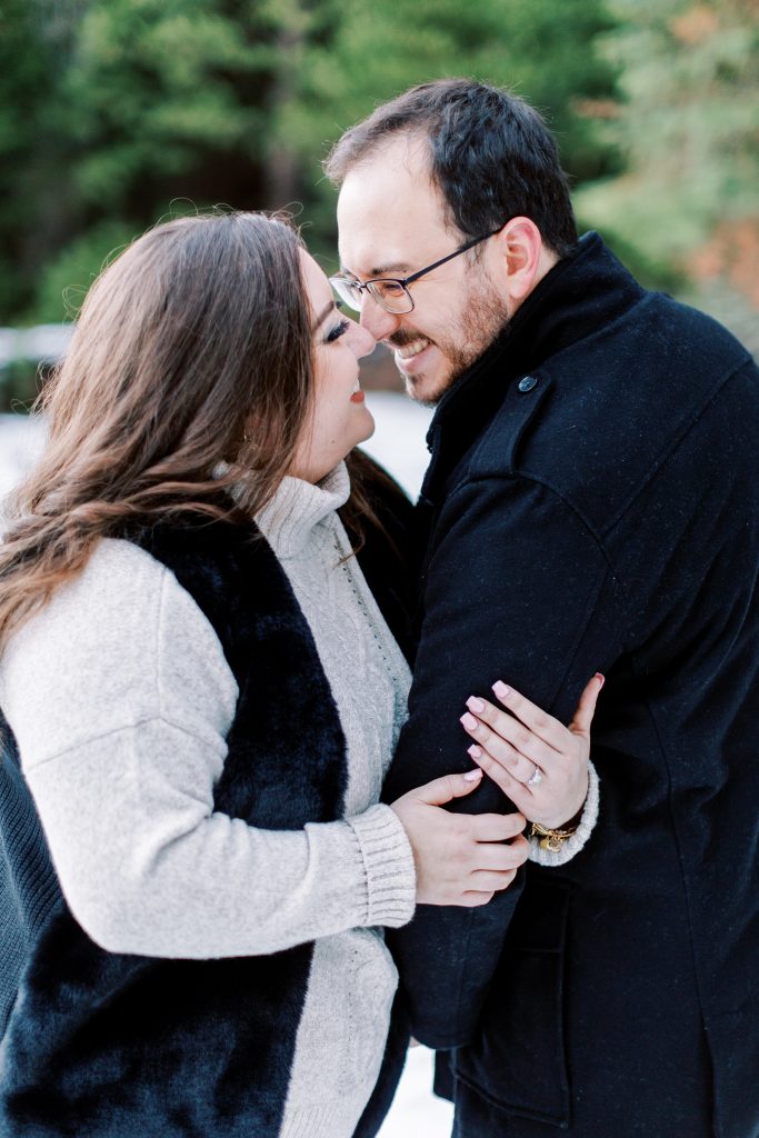 engaged couple in black and grey touching noses and smiling for a snowy winter engagement session