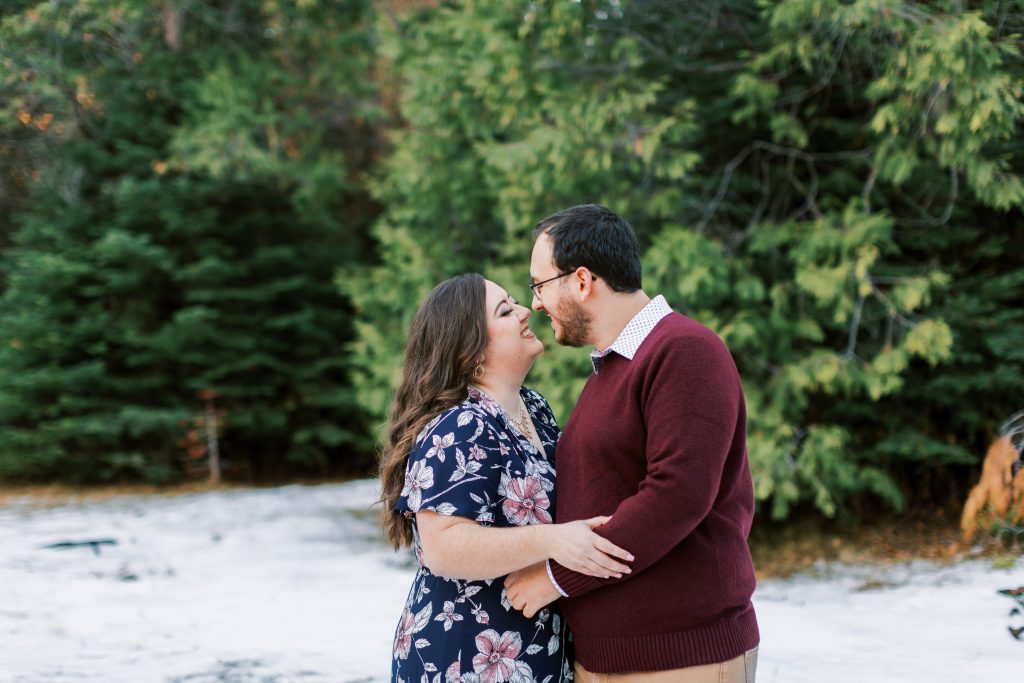 engaged couple wearing navy and maroon embracing in a snowy mountain meadow