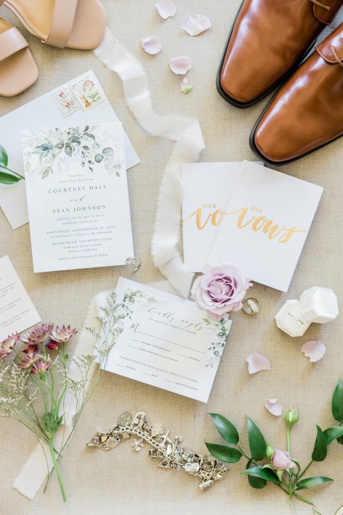 Invitations, shoes, vow books, rings, and flowers laid out from wedding
