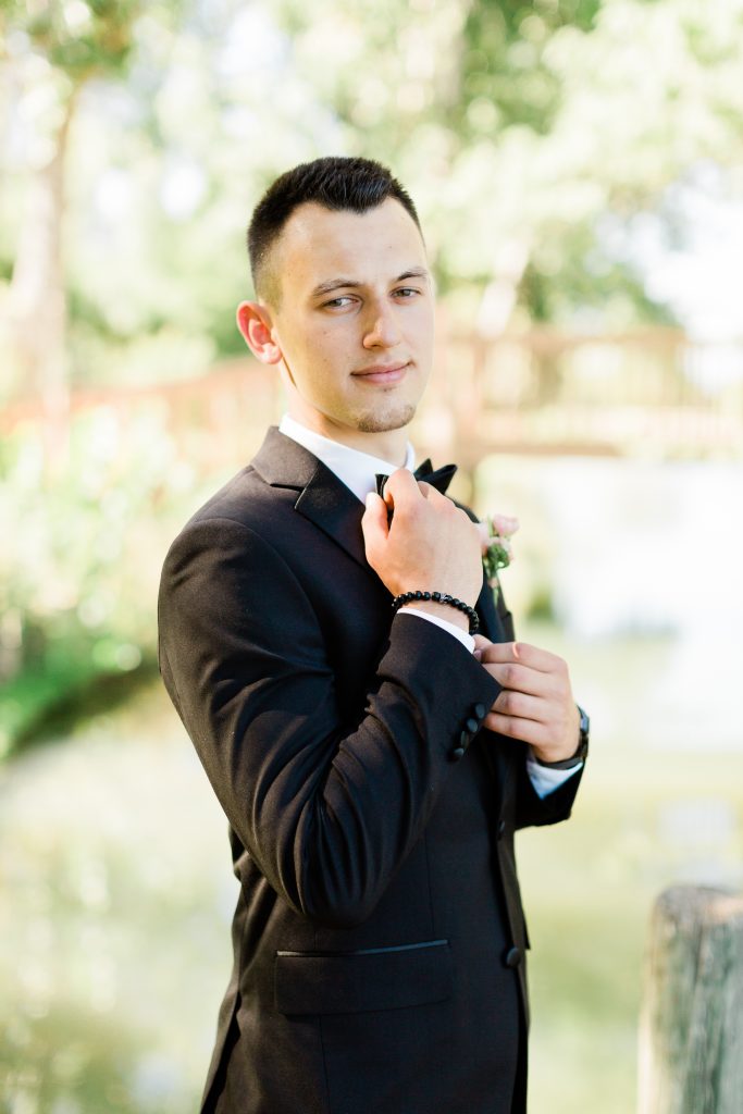 groom in a black tuxedo adjusting his bow tie 