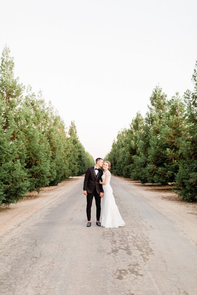 bride and groom standing on a road along the driveway at wolf lakes lined with trees