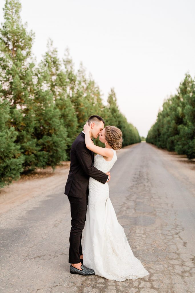 bride and groom kissing along the driveway lined with trees at wolf lakes by fresno wedding photographer megan helm