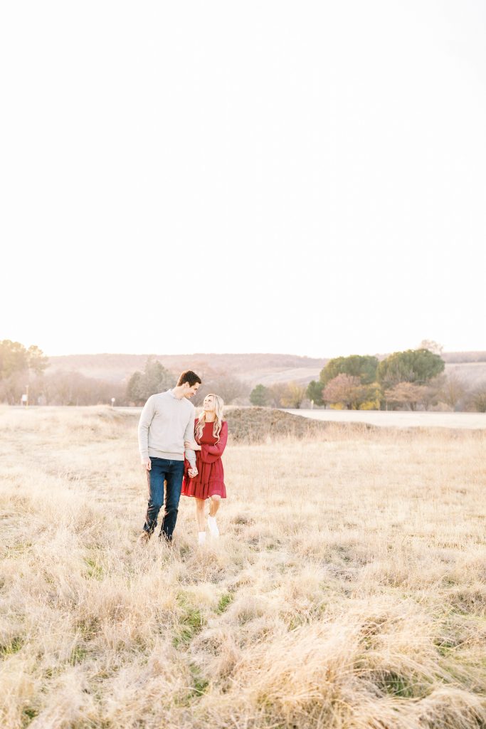 engaged couple walking through a golden grassy field