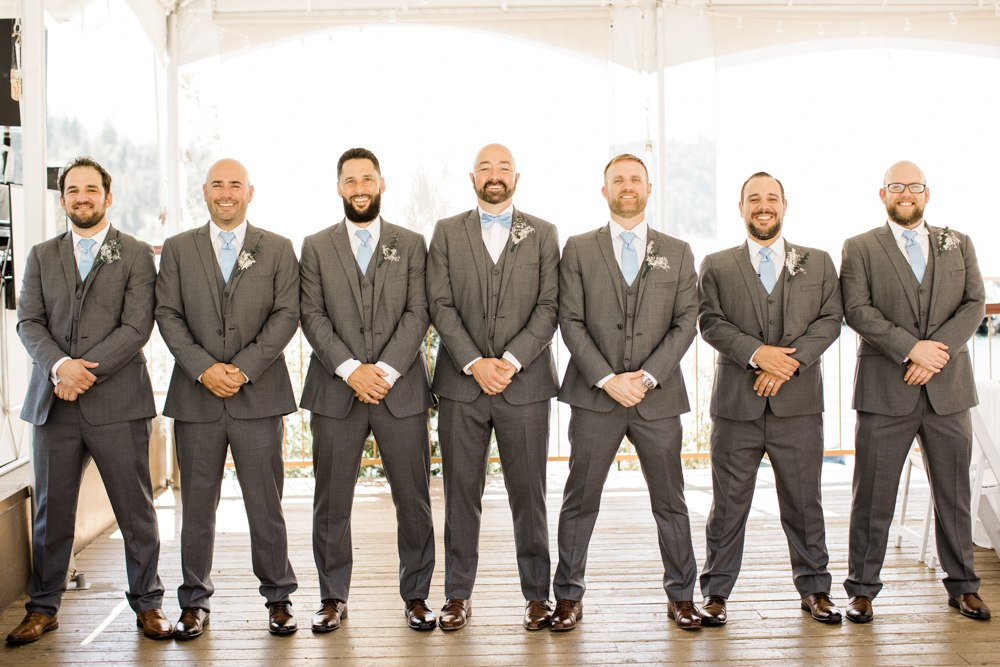 Groomsmen lined up and smiling in grey suits with blue ties