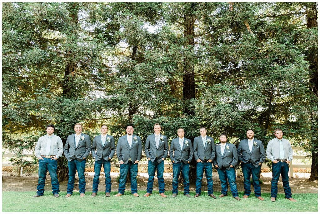 Groomsmen in grey and jeans standing in front of tall trees