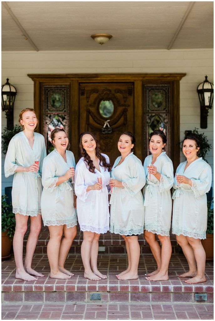 bride and bridesmaids in teal and white robes standing in a line with mimosas