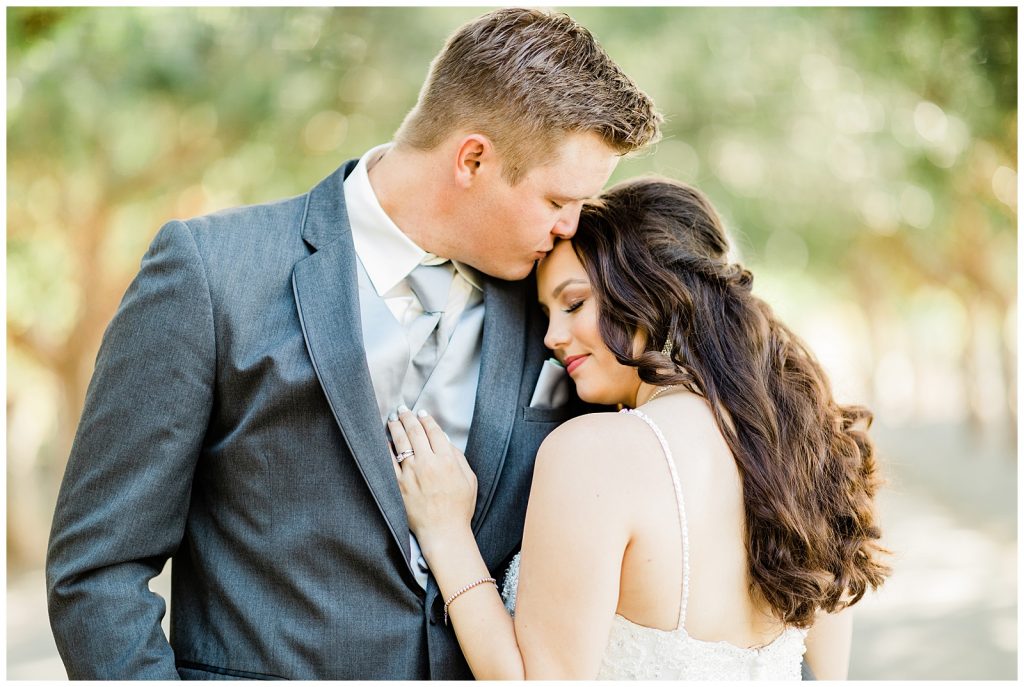 Bride leaning on Grooms chest while he kisses her forehead