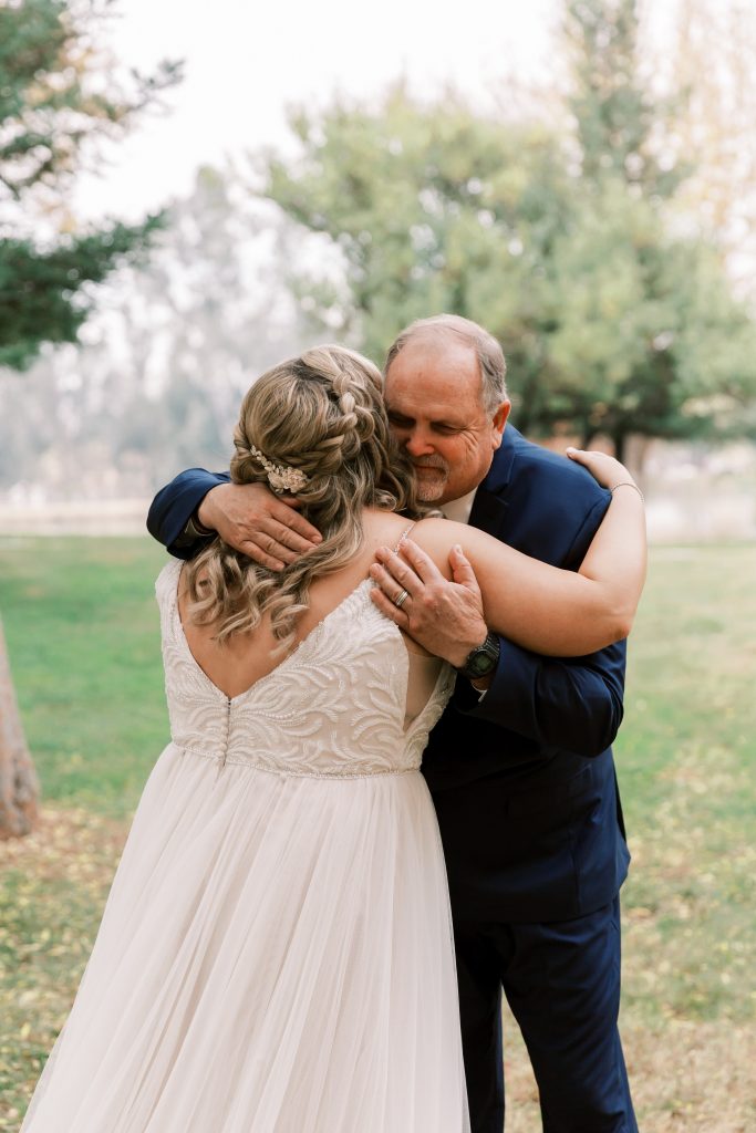 Bride and her dad hugging in joy outside on an overcast wedding day at wolf lakes park a fresno wedding venue