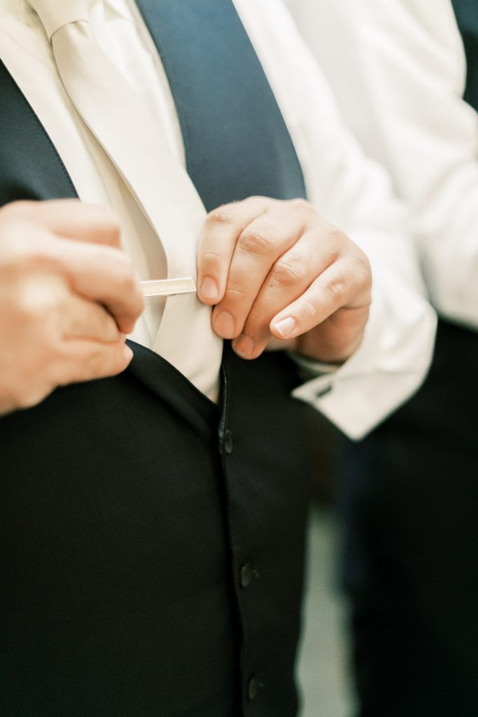 Close up of groom putting on his custom tie clip